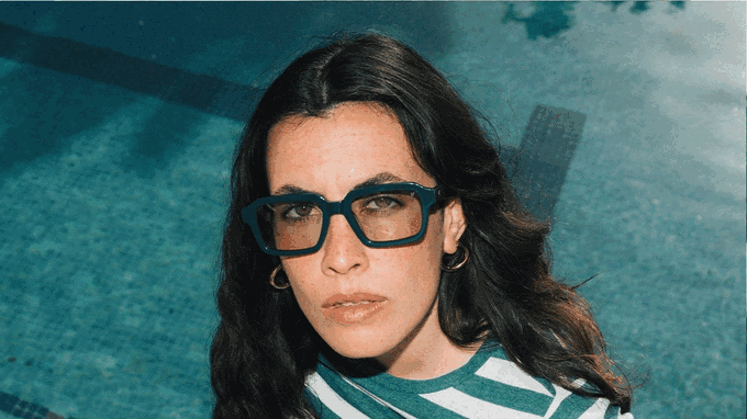 Una mujer con las gafas puestas junto a una piscina, a pleno sol